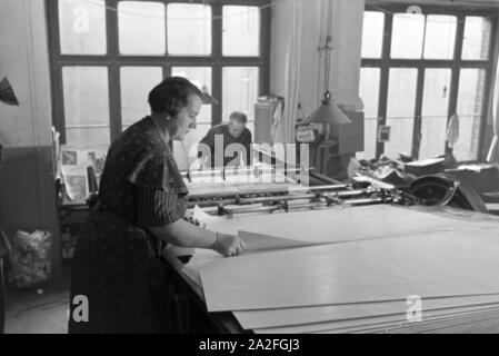 Eine Druckereimitarbeiterin legt die bedruckten Papierbögen in eine Planschneidemaschine produziert vom Maschinenbaukonzern MAN (Maschinenfabrik Augsburg-Nürnberg), Deutschland 1930er Jahre. Un lavoratore in una printery sta mettendo la carta stampata in fogli all'interno di una macchina di taglio, che viene prodotta mediante l'ingegneria meccanica azienda MAN (Maschinenfabrik Augsburg-Nürnberg), Germania 1930s. Foto Stock