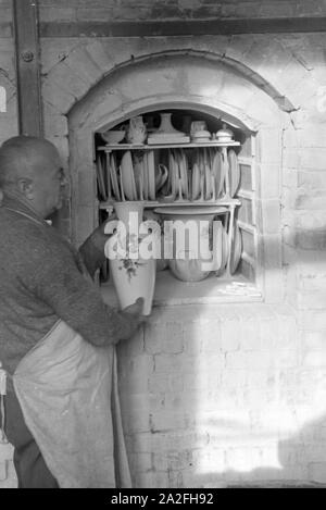 Ein Keramiker der Staatlichen Porzellanmanufaktur Berlin stellt eine bemalte vaso in den Brennofen für den Glattbrand, Deutschland 1930er Jahre. Un ceramista dello Stato manifattura di porcellana Berlin mette un vaso verniciato all'interno del forno per la bicottura, Germania 1930s. Foto Stock