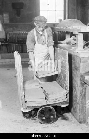 Ein Keramiker der Staatlichen Porzellanmanufaktur Berlin sortiert rohe Keramikplatten für den Schrühbrand, Deutschland 1930er Jahre. Un ceramisti di stato manifattura di porcellana Berlin ordina materie di piastre in ceramica per il bisque cottura, Germania 1930s. Foto Stock