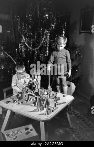 Zwei Jungen spielen am Weihnachtsabend mit den neuen Bauklötzen, Deutschland 1938. Due ragazzi giocare con il nuovo set di blocchi giocattolo sotto l albero di natale, Germania 1930 Foto Stock