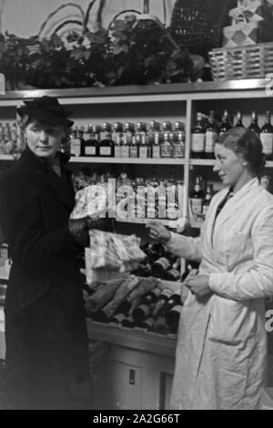 Eine Frau läßt sich bei ihren Weihnachtseinkäufen von der Verkäuferin in der Spiritousenabteilun in einem Kaufhaus beraten, Deutschland 1930er Jahre. Una donna facendo il suo shopping natalizio e ottiene alcune raccomandazioni da parte di un addetto ad una departement store, Germania 1930s. Foto Stock