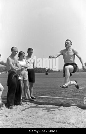 Übung im Weitsprung auf dem Sportplatz des KdF Sportheim Belzig in der Mark Brandenburg, Deutschland 1930er Jahre. Salto in lungo esercizio presso il campo sportivo dello sports club house a Belzig nel Brandeburgo, Germania 1930s. Foto Stock