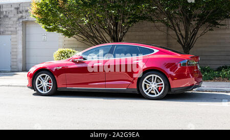 Vista laterale di una Tesla Model S rossa parcheggiata sul lato di una strada durante una giornata di sole. Foto Stock