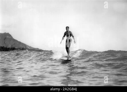 Medaglia d'oro olimpica nuotatore e padre della moderna Surf, Duke Kahanamoku, a cavallo di un onda su una tavola da surf in legno in Waikiki Hawaii con testa di diamante in background. Foto Stock