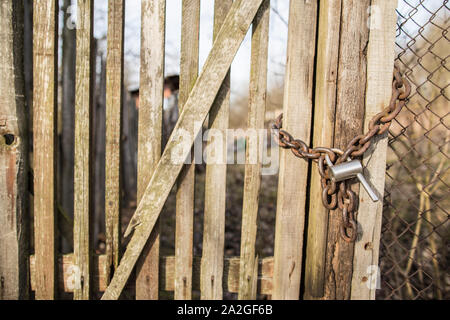 Chiuso cancello in legno con il vecchio arrugginito catena e lucchetto, molla giornata di sole. Foto Stock