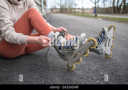 Ragazza seduta sulla strada e la legatura dei lacci su pattini a rotelle, close-up. Concetto: sport, uno stile di vita sano. Foto Stock