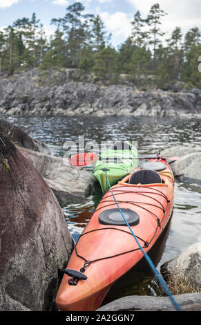 Due kayak stand ormeggiata su una spiaggia sassosa, sullo sfondo di una scogliera, della foresta e del cielo. Foto Stock