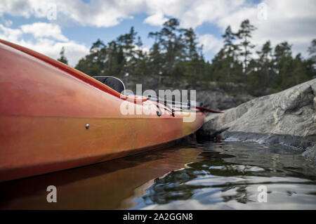 Kayak sta ormeggiata su una spiaggia sassosa, sullo sfondo di una scogliera, della foresta e del cielo. Foto Stock