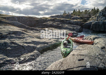 Due kayak vengono ormeggiate sulla spiaggia rocciosa, sullo sfondo è possibile vedere il vecchio ponte di legno, cielo nuvoloso e foresta. Foto Stock