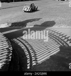 Ein Auto parkt in der Sonne, davor die Schatten des schmiedeeisernen Zaunes der Orangerie a Fulda, Deutschland 1930erJahre. Un parcheggio auto al sole di fronte l'ombra del ferro battuto recinzione di Fulda aranciera, Germania 1930s. Foto Stock