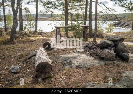 Il campeggio sul litorale roccioso del lago. Un vecchio tavolo di legno, un banco di registri e di un posto per un incendio tra i pini. Foto Stock