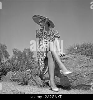 Eine junge Frau sitzt in einem Sommerkleid auf einem Felsen, Deutschland 1930er Jahre. Una giovane donna che indossa un vestito estivo seduto su una roccia, Deutschland 1930s. Foto Stock