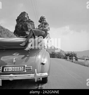 Eine junge Frau sitzt mit ein paar Zweigen auf dem Faltdach eines Opel Cabrio, Österreich 1930er Jahre. Una giovane donna con lop sul tetto apribile di una Opel cabrio, Austria 1930s. Foto Stock