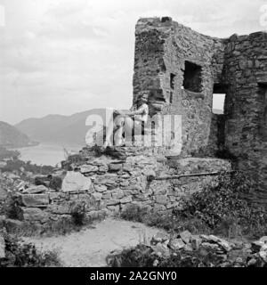 Eine junge Frau sitzt in einer Ruine Un einem Fluß, Österreich, 1930er Jahre. Una giovane donna seduta nei resti di un antico castello, Austria 1930s. Foto Stock