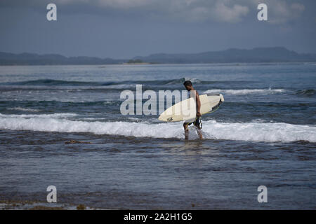 Un surfista tornando a piedi a terra dopo una sessione di navigazione al Cloud 9 surf break,Siargao,Filippine Foto Stock
