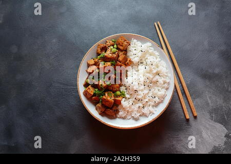 Tofu dolce, piccante, croccante e fritto in salsa teriyaki servito in una ciotola con semi di sesamo e riso. Cibo vegano sano, senza glutine Foto Stock