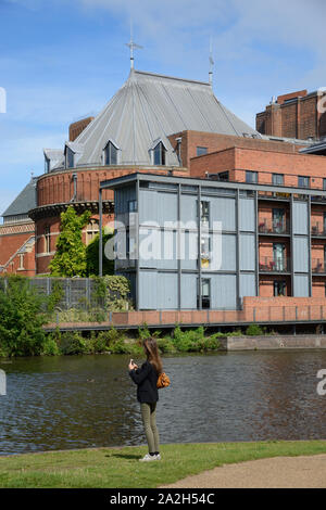 Giovane donna prendendo fotografie sulle rive del fiume Avon di fronte al Royal Shakespeare Theatre o al teatro di Stratford-upon-Avon Inghilterra Foto Stock