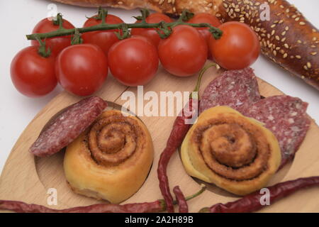 Gustoso cibo essiccato peperoncino pomodori ciliegia, prosciutto e piccolo pane sul piatto di legno su sfondo bianco. Foto Stock