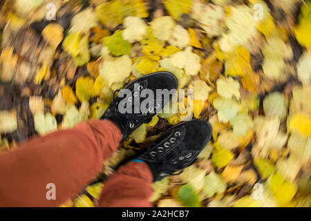 Un uomo in camoscio nero scarpe e pantaloni rossi sorge sul Giallo autunno caduta foglie di un albero di tiglio, una sfocatura in movimento in un cerchio. Foto Stock