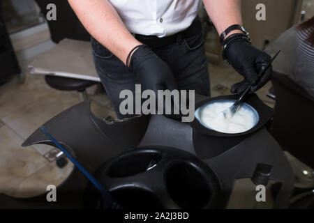 Stylist maschio nel preparare i guanti color crema per morire hairin un contenitore, una maschera per il procedimento di trattamento in un salone di bellezza. Hhairdresser spazzola di miscelazione Foto Stock