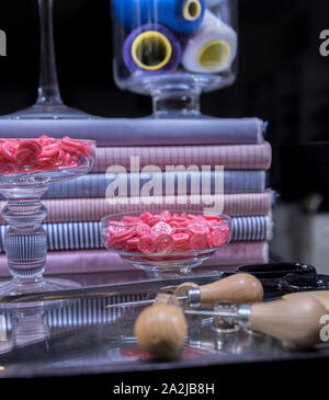 Sartoriale forbici, AWL, gesso e ditale presentata sul tavolo di vetro circondato da pulsanti e tessuto della camicia Foto Stock