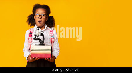 Americano africano studente elementari che trasportano microscopio e pila di libri Foto Stock