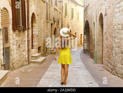 Visto da dietro del turista donna in abito giallo e cappello visitando antiche città italiane. Foto Stock