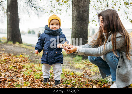 Carino baby boy nel quartiere alla moda di abbigliamento casual esplora il mondo con la madre in autunno la natura park Foto Stock