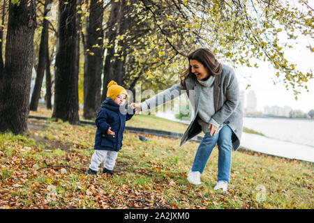 Carino baby boy nel quartiere alla moda di abbigliamento casual esplora il mondo con la madre in autunno la natura park Foto Stock