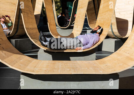 Un visitatore si rilassa sul si prega di essere insediato l'installazione da Paul Cocksedge presso il London Design Festival 2019, Finsbury Avenue Square, Broadgate, Londra Foto Stock