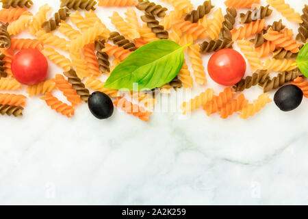 Il cibo italiano sfondo. Fusilli con olive nere, pomodorini e una foglia di basilico, girato dalla parte superiore su un marmo bianco sullo sfondo Foto Stock