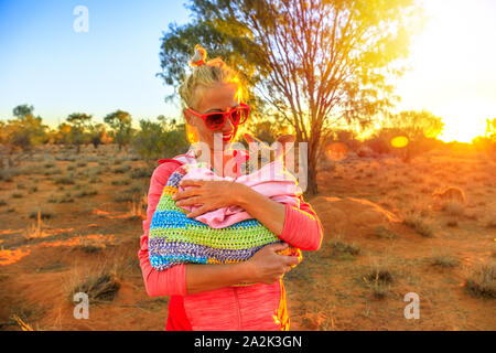 Donna turistica azienda di orfani baby kangaroo al tramonto del sole nel outback australiano. Interagire con graziosi kangaroo orfano. Marsupiale australiano in Foto Stock