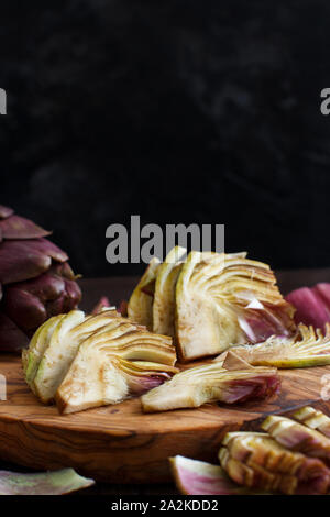 Carciofi romani su una tavola di legno su uno sfondo scuro Foto Stock