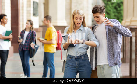 Gli studenti nei campus universitari guardando orologi Foto Stock