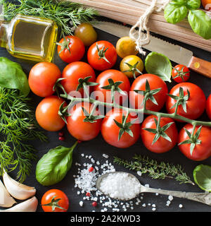 La cucina italiana ingridients : pomodori ciliegia, erbe, pasta e olio d'oliva su sfondo scuro Foto Stock