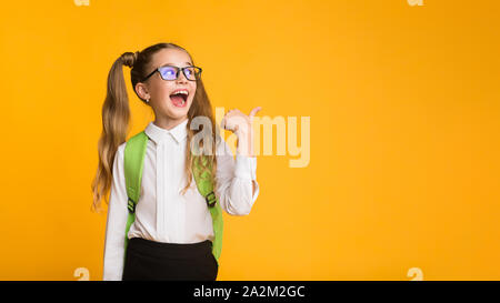 Eccitato studente elementare puntando il pollice a Copyspace su sfondo giallo Foto Stock