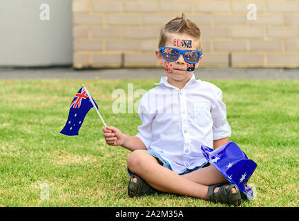 Australian ragazzo che indossa un cappello e occhiali da sole seduti sul prato verde durante l'Australia Day celebrazione Foto Stock
