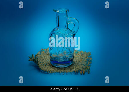 Blu di vetro modellato decanter su un quadrato di hessian evidenziato su una corrispondente sfondo blu con vignette e spazio di copia Foto Stock