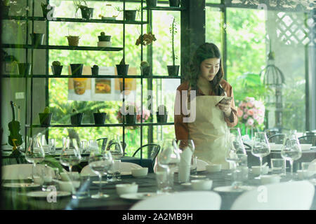 Pmi donna giovane proprietario del ristorante tramite telefono cellulare shot throught finestra. Foto Stock