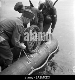 Original-Bildunterschrift: Kableverlegung durch einen Fluß - der Kabelwagen wird auf dem Boot befestigt, Deutschland 1940er Jahre. Installare i fili sul Fiume - il tamburo del cavo viene caricato per la barca in gomma, Germania 1940s. Foto Stock