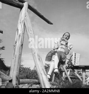 Eine junge Frau sitzt Mit einem Akkordeon un einem Zaun, Deutschland 1930er Jahre. Una giovane donna seduta da un recinto con una fisarmonica Germania 1930s. Foto Stock