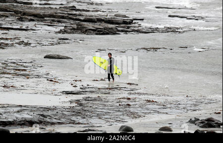 Un surfista lascia l'acqua in Lahinch, County Clare, sulla costa occidentale dell'Irlanda come tempesta Lorenzo è previsto di fare approdo, con uno stato di colore arancione del vento e di avvertimento giallo di avvertimento di pioggia che è stato rilasciato. Foto Stock