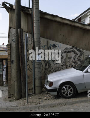 Parte anteriore del bianco auto Mercedes in parte anteriore del vecchio edificio con muro di graffiti Foto Stock