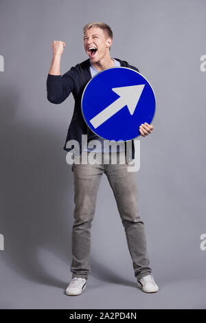 Overjoyed uomo azienda round cartello blu con la freccia. Foto Stock
