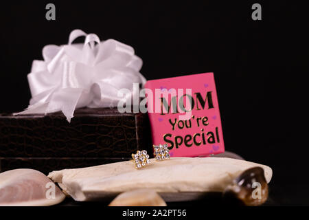 Bella Orecchini diamante su pietra con mom sei mini speciale messaggio prenota e decorata in pelle marrone box su sfondo nero. La festa della mamma regalo c Foto Stock