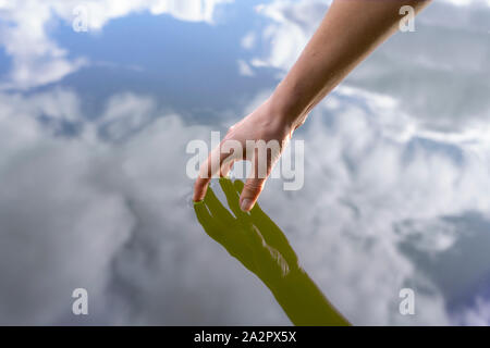 Womans aveva toccando la superficie di un lago, riflessioni di mano e cielo Foto Stock