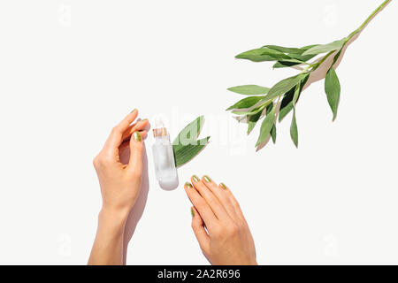 Bottiglia di olio cosmetico accanto a mani femminili con verde manicure e foglie fresche su sfondo bianco con copia spazio, piatto composizione laici. Foto Stock