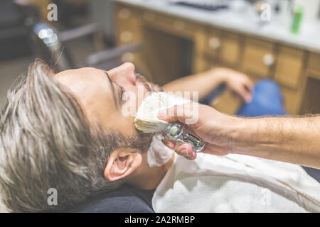 Parrucchiere professionale applicazione di schiuma da barba sulla pelle del client in barberia. Foto Stock