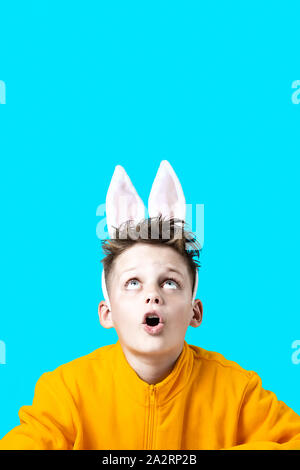 Ragazzo sorpreso in una giacca gialla e le orecchie di lepre su uno sfondo blu Foto Stock