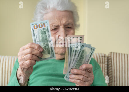 Un senior donna cercando di dollari americani nella sua mano rugosa Foto Stock